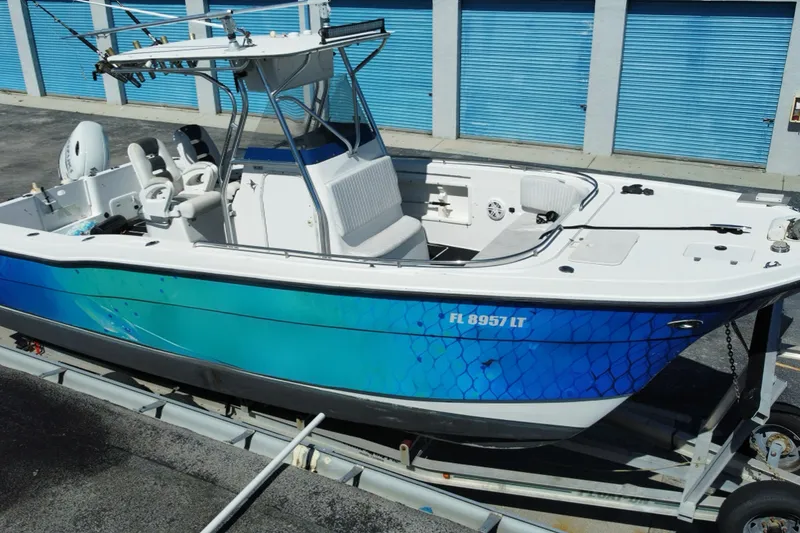 Slide: The Image of 2002 ProKat 2660 Center Console boat with blue hull on trailer, parked near storage units. - 19