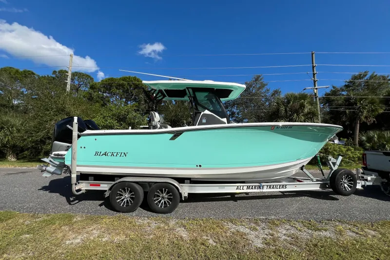 Slide: The Image of 2023 Blackfin 272 boat on trailer, parked outdoors under clear blue sky. - 0