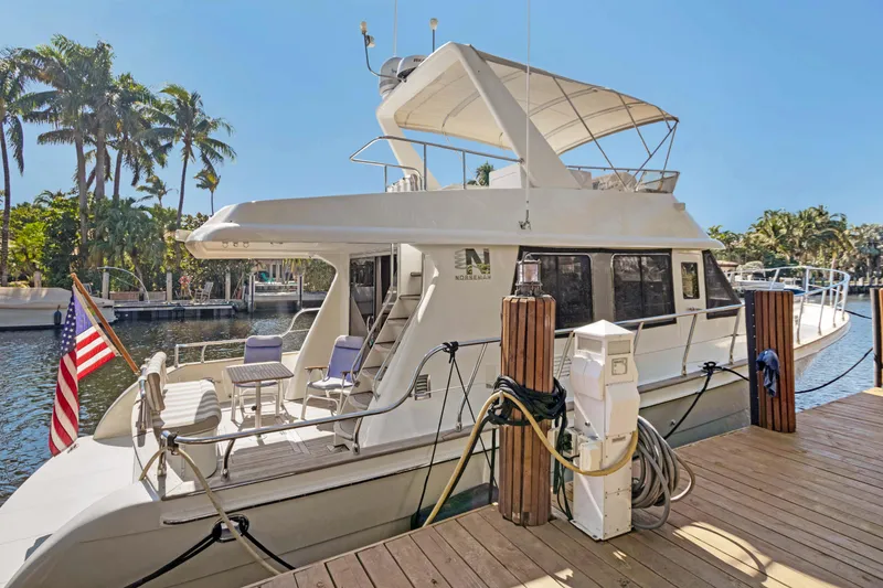 Slide: The Image of 2006 Noresman 480 Sedan yacht docked, featuring outdoor seating and American flag. - 70