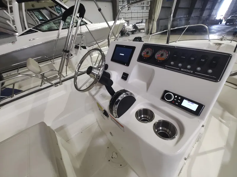 Slide: The Image of 2022 Boston Whaler 190 Montauk boat console with steering wheel and gauges in a marina. - 21