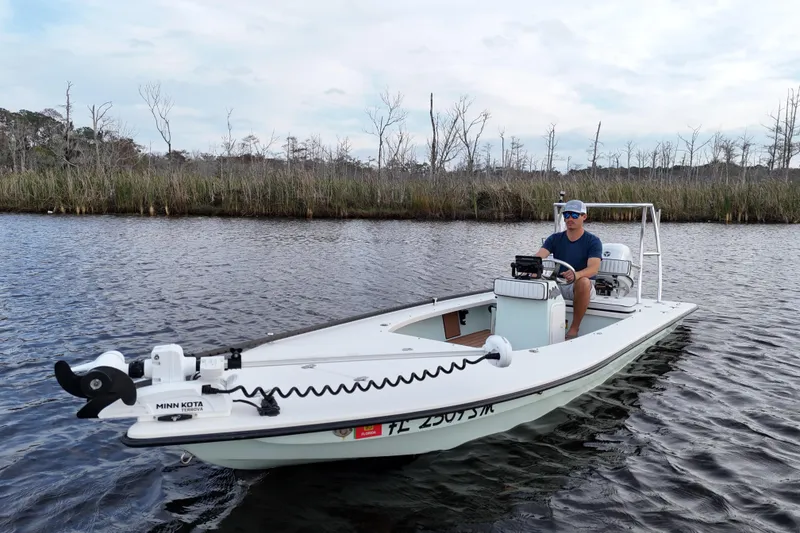 Slide: The Image of 2019 Skimmer Skiff 16'6" CC boat on water with person steering, surrounded by marshland. - 24