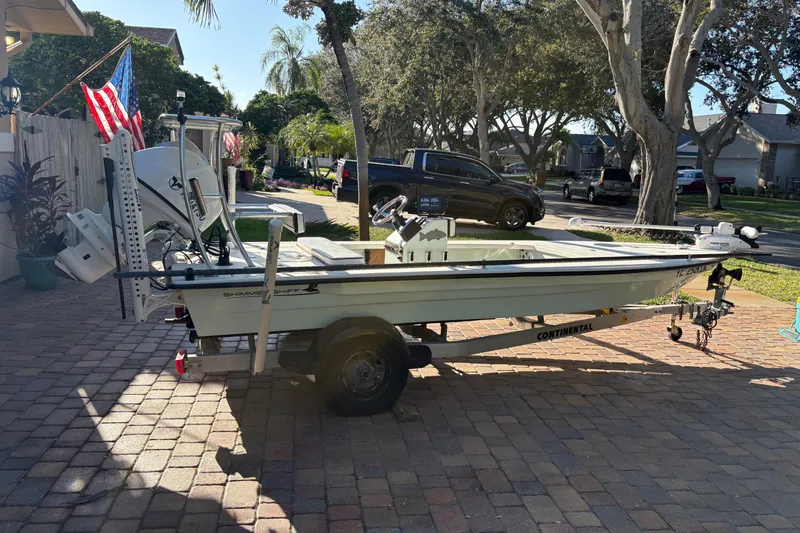 Slide: The Image of 2019 Skimmer Skiff 16'6" CC boat on trailer, parked in a driveway with trees and flags. - 40