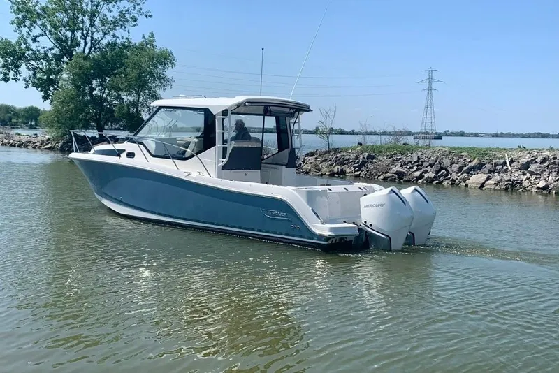 Slide: The Image of 2022 Boston Whaler 325 Conquest boat cruising on a calm lake near a rocky shoreline. - 1