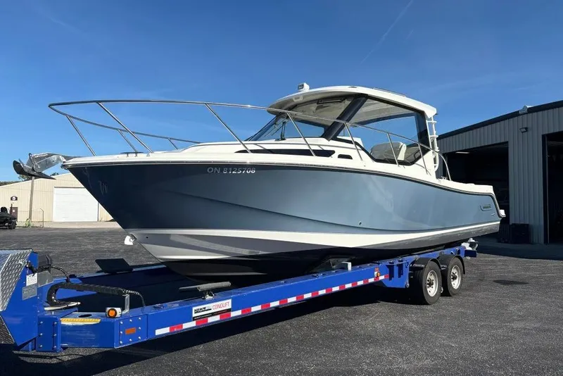 Slide: The Image of 2022 Boston Whaler 325 Conquest boat on trailer, parked outside a warehouse. - 2