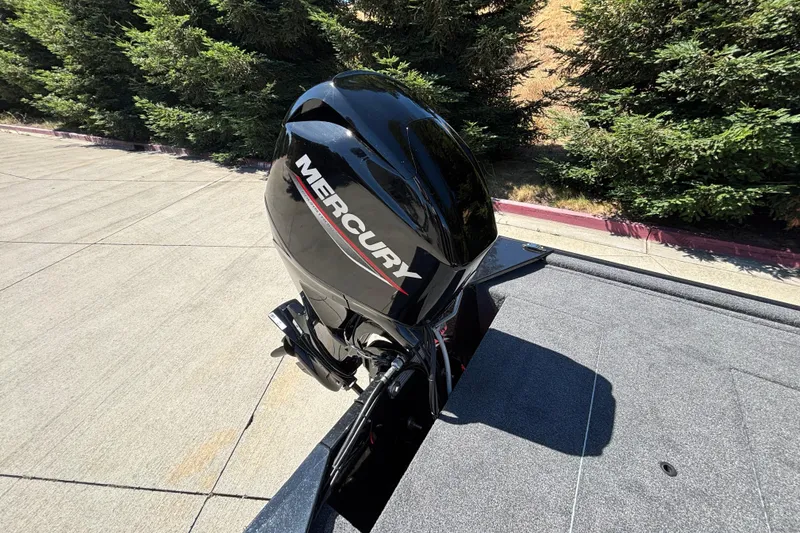 Slide: The Image of 2026 Tracker Bass Tracker Classic XL with Mercury outboard motor, parked near trees. - 6