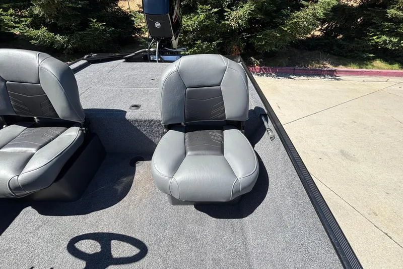 Slide: The Image of 2026 Tracker Bass Tracker Classic XL boat seats on a carpeted deck, surrounded by trees. - 13