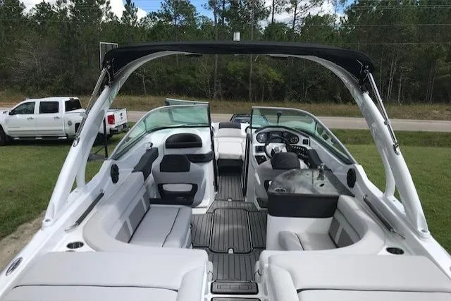 Slide: The Image of 2018 Rinker 29QX boat interior with seating and dashboard, parked on grass. - 9
