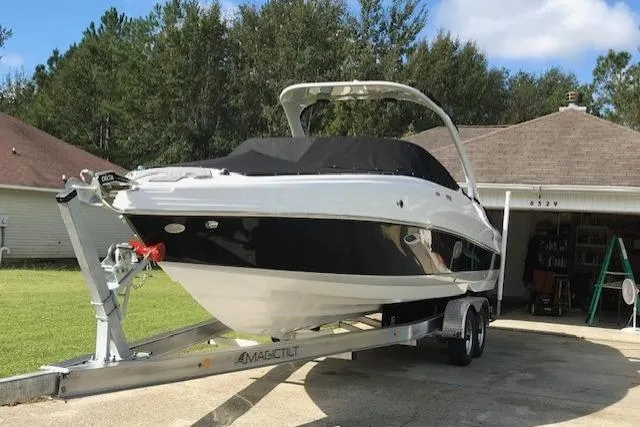 Slide: The Image of 2018 Rinker 29QX boat on trailer in driveway, surrounded by trees and houses. - 1