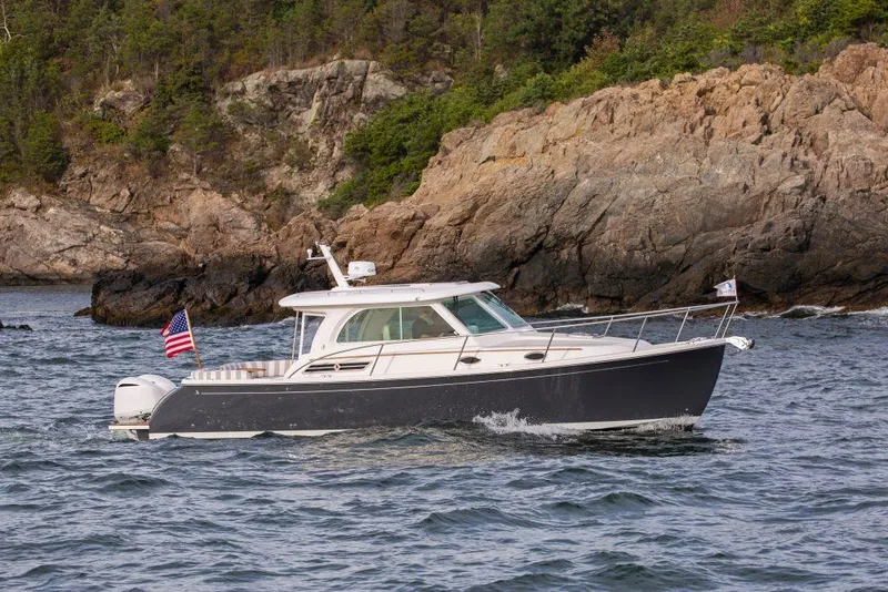 Slide: The Image of 2026 Back Cove 340 cruising near rocky shoreline with American flag. - 4