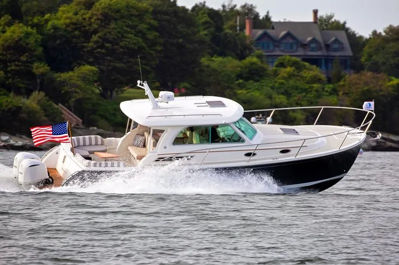 Slide: The Image of 2026 Back Cove 340 cruising on water with American flag, surrounded by lush greenery. - 24