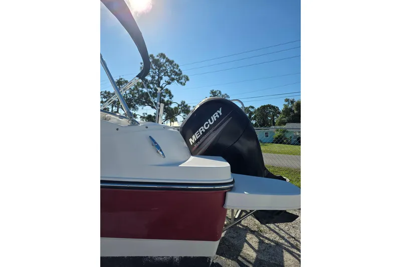 Slide: The Image of 2013 Bayliner 190 Deck Boat with Mercury outboard motor, parked outdoors under clear blue sky. - 3