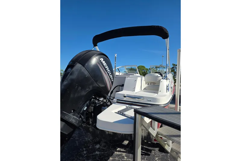 Slide: The Image of 2013 Bayliner 190 Deck Boat with Mercury outboard engine, docked under clear blue sky. - 4
