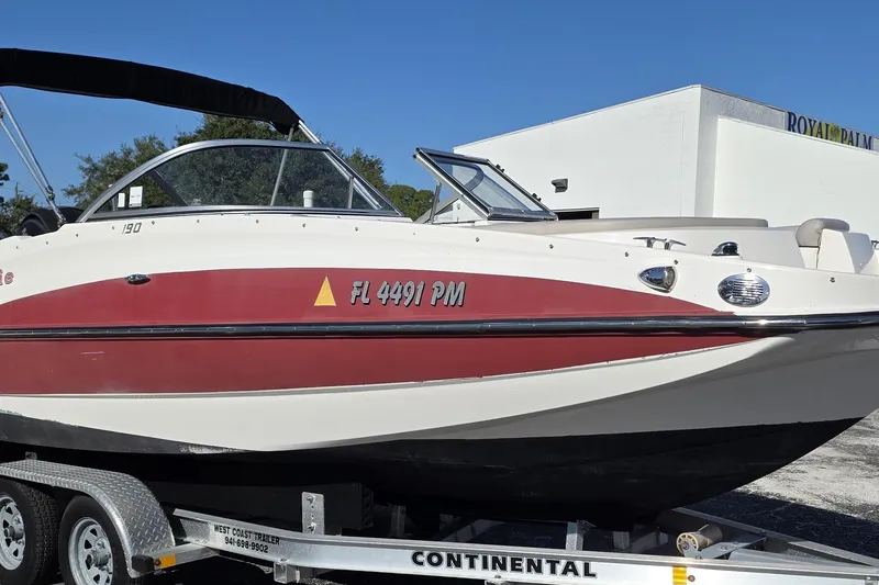 Slide: The Image of 2013 Bayliner 190 Deck Boat on trailer, red and white design, parked outdoors. - 5