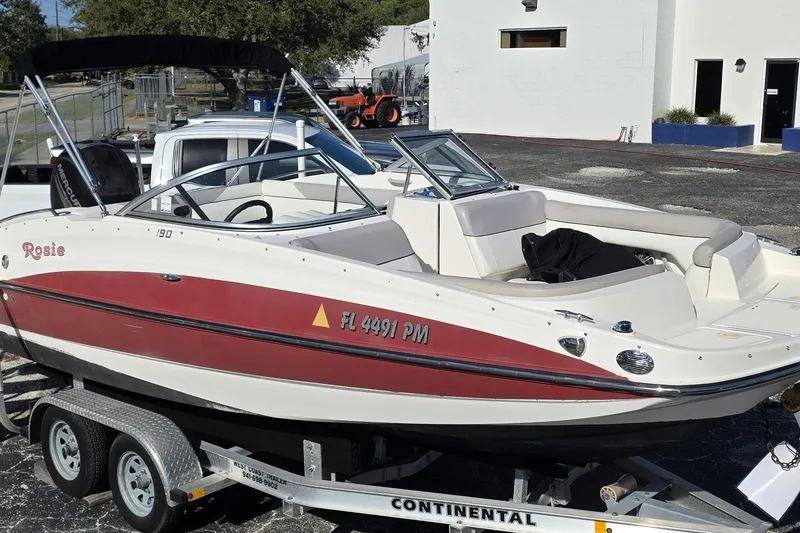 Slide: The Image of 2013 Bayliner 190 Deck Boat on trailer, red and white design, parked outdoors. - 6