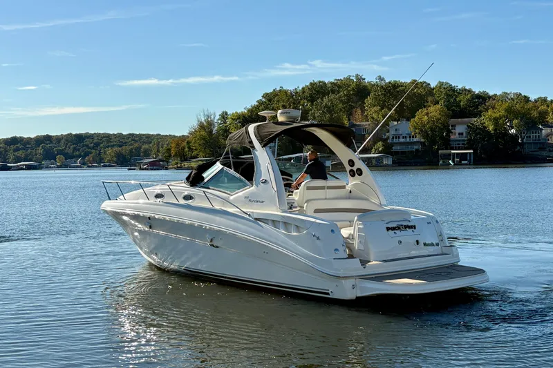 Slide: The Image of 2004 Sea Ray 320 Sundancer cruising on a serene lake with lush green shoreline. - 2