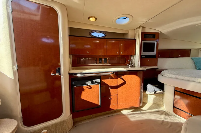 Slide: The Image of 2004 Sea Ray 320 Sundancer cabin interior with wood cabinetry, compact kitchen, and cozy seating area. - 34