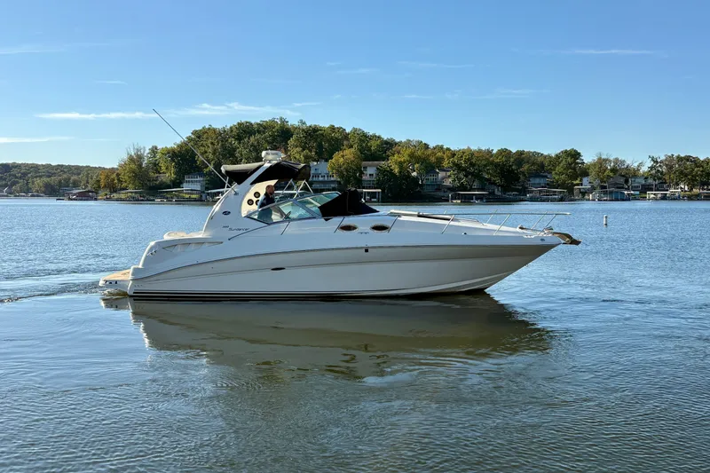 Slide: The Image of 2004 Sea Ray 320 Sundancer cruising on a serene lake with lush green shoreline. - 5