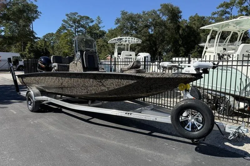 Slide: The Image of 2026 Xpress H20B Bay boat on trailer, parked outdoors with trees in background. - 2