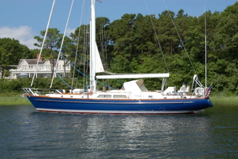 The Image of 1983 Camper & Nicholsons Cutter Rig sailboat on calm water, surrounded by lush greenery. - 0