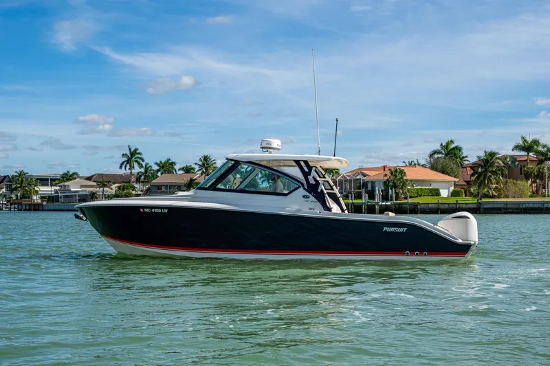 Slide: The Image of 2017 Pursuit DC 295 Dual Console boat on calm water, with houses and palm trees in the background. - 17