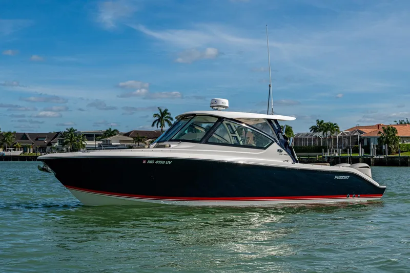 Slide: The Image of 2017 Pursuit DC 295 Dual Console boat on calm water, with houses in the background. - 19
