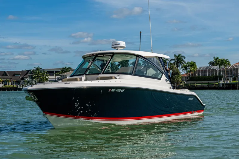 Slide: The Image of 2017 Pursuit DC 295 Dual Console boat on calm water, with coastal homes in the background. - 20