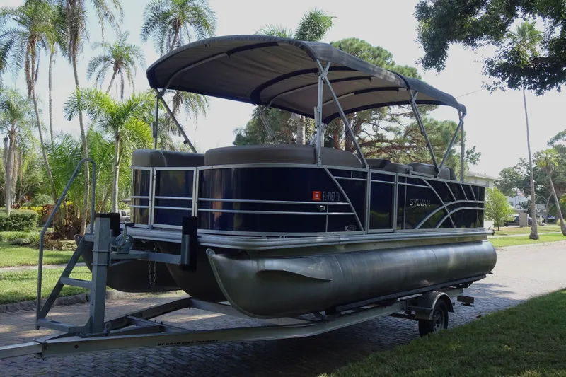 Slide: The Image of 2023 Sylvan Mirage Fish 820 Party Fish pontoon boat on trailer, surrounded by palm trees. - 6