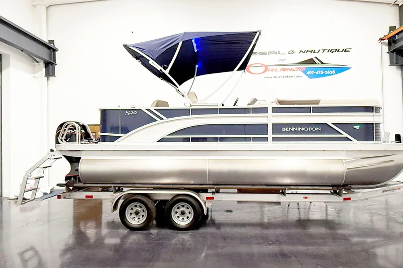 The Image of 2025 Bennington 20S pontoon boat with blue canopy on trailer in showroom. - 1