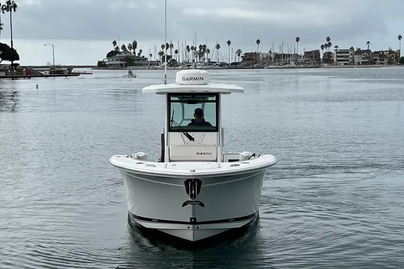Slide: The Image of 2019 Blackfin 272 CC boat on calm water, with coastal buildings in the background. - 2