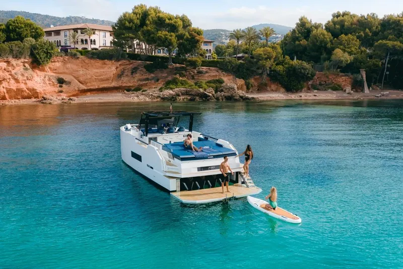 Slide: The Image of 2026 De Antonio Yachts 50 Open in serene bay with people enjoying water activities. - 11