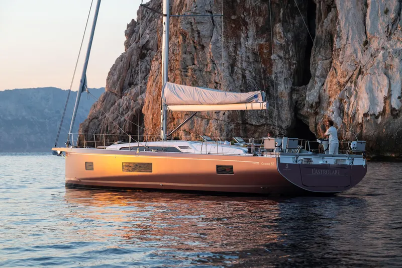 Slide: The Image of 2026 Beneteau Oceanis 52 yacht sailing near rocky cliffs at sunset. - 12