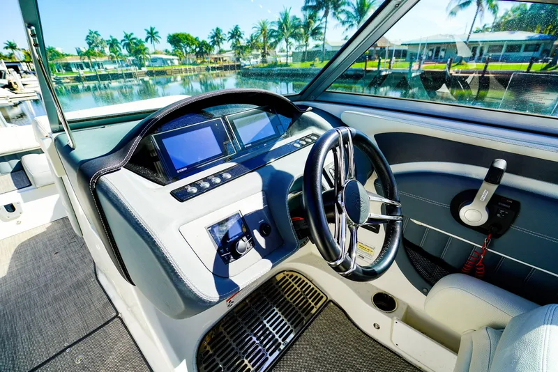 Slide: The Image of 2019 Cobalt 23SC boat dashboard with steering wheel and digital displays, docked by palm trees. - 16