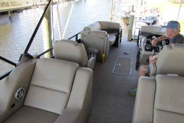 Slide: The Image of 2018 Regency 220 DL3 pontoon boat interior with beige seating and a person at the helm. - 7