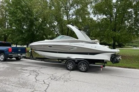 Slide: The Image of 2023 Crownline 260 SS boat on trailer, parked on a tree-lined street. - 1