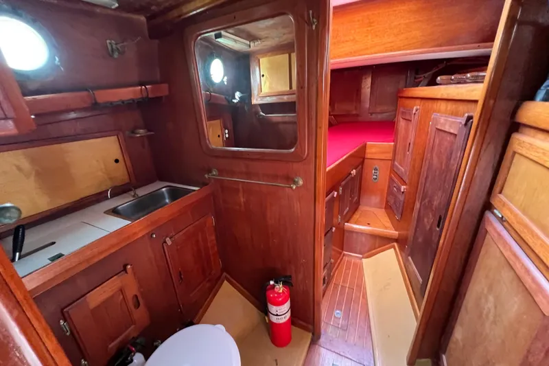 Slide: The Image of 1976 Westsail 32 interior with wooden cabinetry and porthole, featuring red bedding. - 54