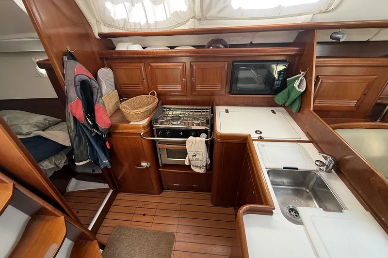 Slide: The Image of Interior of 2005 Beneteau Oceanis 373 sailboat, featuring a compact kitchen with wood cabinetry. - 43