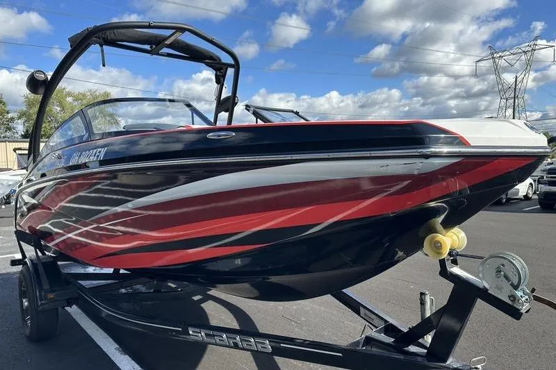 Slide: The Image of 2016 Scarab 195 H.O. boat on trailer, red and black design, under blue sky. - 6