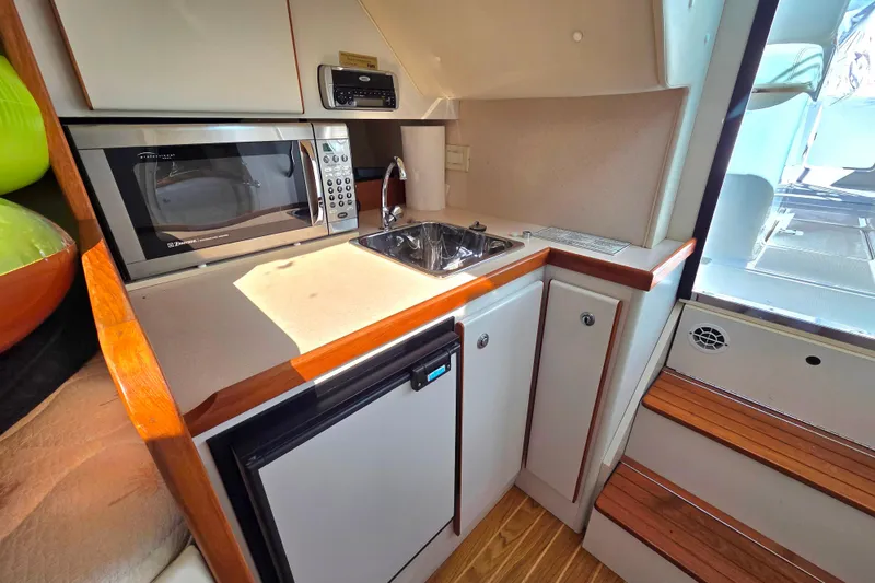 Slide: The Image of Compact kitchen area in a 2004 Tiara 29 Coronet Harbor Edition boat, featuring a microwave and sink. - 13