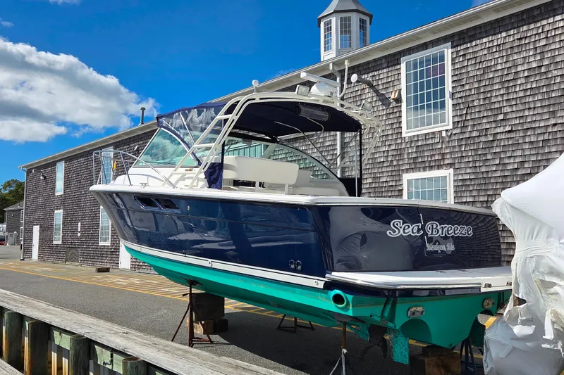 Slide: The Image of 2004 Tiara 29 Coronet Harbor Edition boat, named "Sea Breeze," docked near a shingled building. - 2