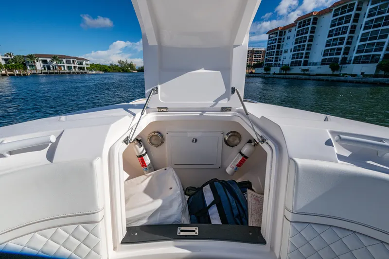 Slide: The Image of 2020 Intrepid 375 Nomad SE boat storage compartment with fire extinguishers, docked near waterfront buildings. - 17