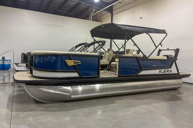The Image of 2026 Alera M23Q pontoon boat with blue panels and canopy in showroom. - 1