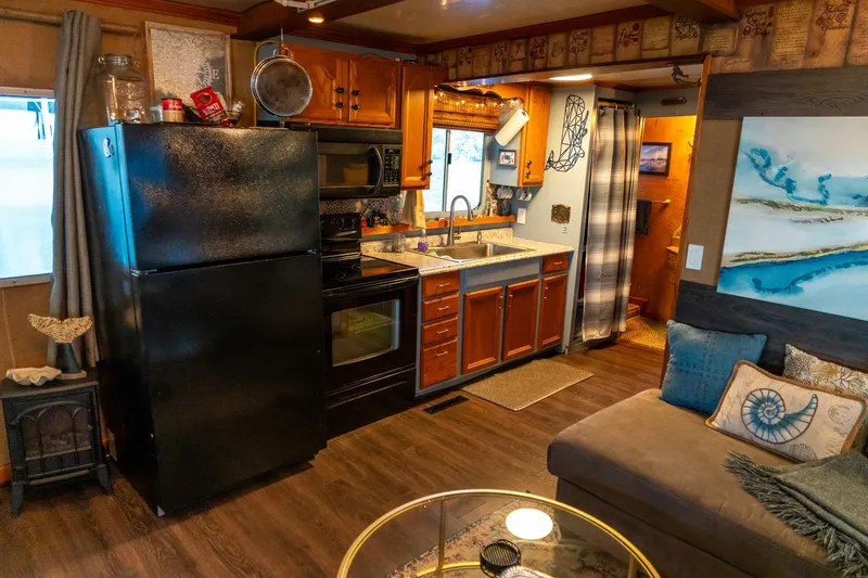 Slide: The Image of Cozy 1989 Seabreeze houseboat kitchen with wooden cabinets, black appliances, and nautical decor. - 14