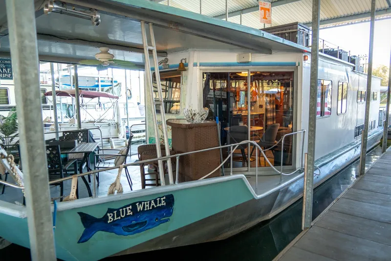 Slide: The Image of 1989 Seabreeze 53 x 14 houseboat docked, named "Blue Whale," with outdoor seating area. - 3