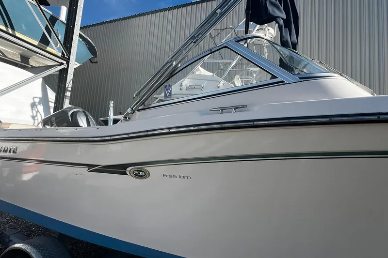 Slide: The Image of 2013 Grady-White Freedom 205 boat, side view, parked near a metal building. - 2