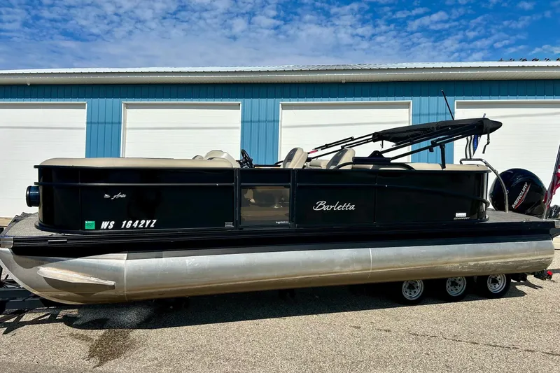 The Image of 2024 Barletta ARIA 22QC pontoon boat on trailer, parked near blue building. - 1