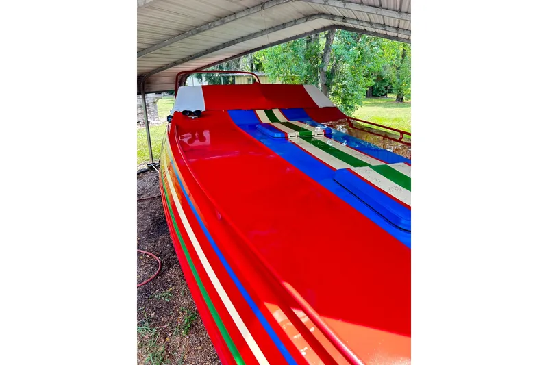 Slide: The Image of 1987 Chris-Craft 312 Stinger boat with vibrant red, blue, and green stripes under a canopy. - 14