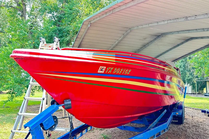 Slide: The Image of 1987 Chris-Craft 312 Stinger boat in vibrant red with colorful stripes, parked under a canopy. - 17