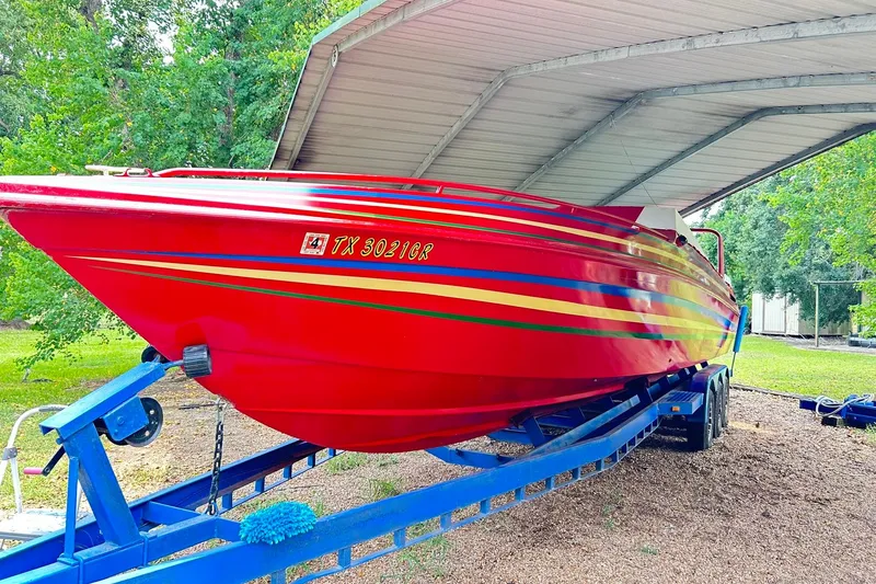 Slide: The Image of 1987 Chris-Craft 312 Stinger boat in vibrant red with colorful stripes, parked on a trailer. - 49