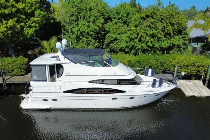 Slide: The Image of 2004 Carver 466 Motor Yacht docked by lush greenery, showcasing sleek design and spacious deck. - 2