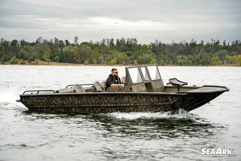 The Image of 2026 SeaArk Predator boat cruising on a lake with forested shoreline. - 1